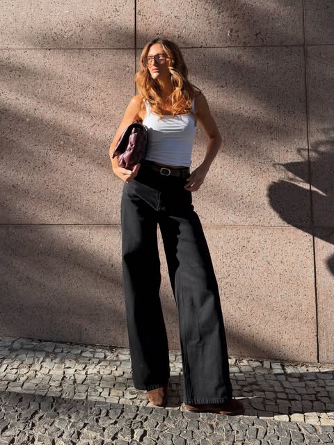 Modelo de calça preta e regata branca na calçada de pedra portuguesa